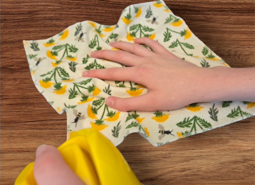 Flannel cloth, yellow flowers and bees on cloth. Picture is showing how product is used to dust a wood surface.